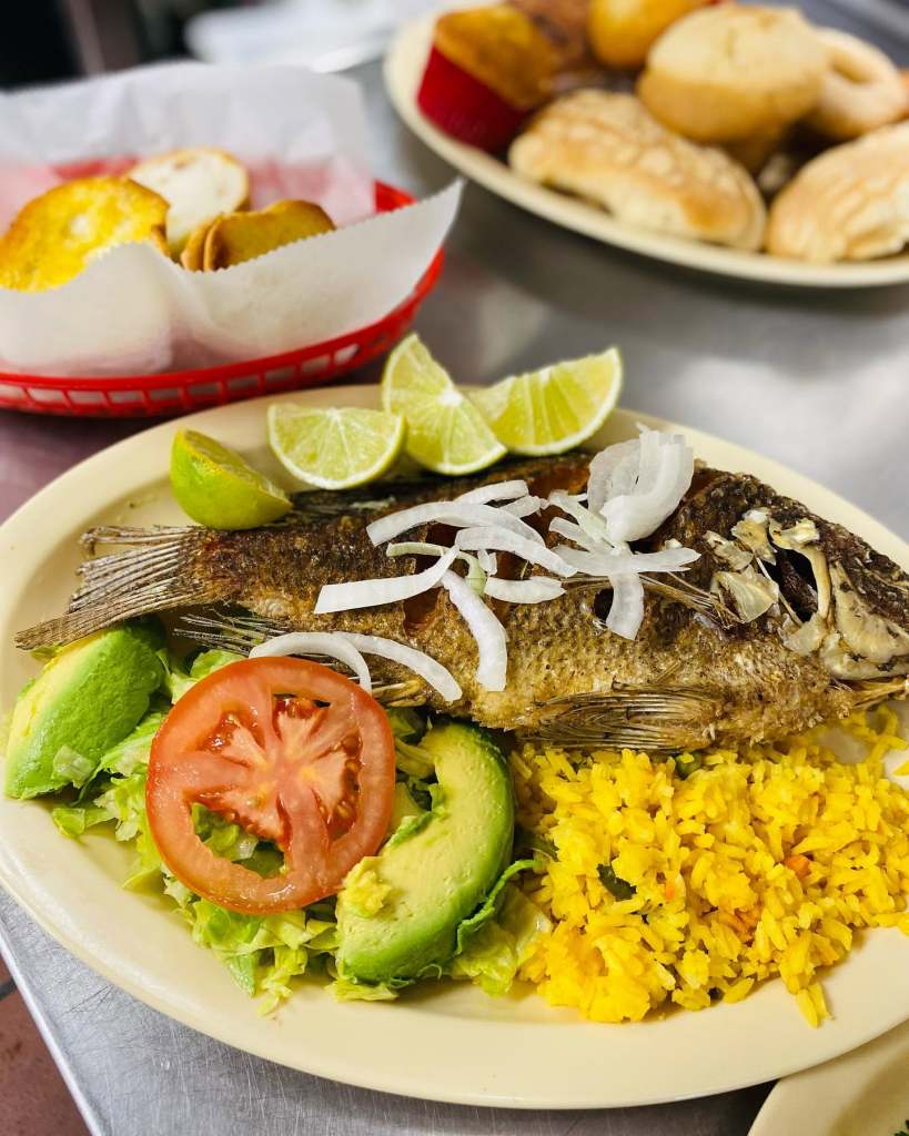 A whole fried fish plate at Tacos El Jaibo, served with yellow rice, fresh avocado, tomato, shredded onion, and lime. Comida casera at its finest.